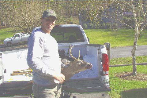 1995 Ford Bronco - A man stands with a harvested deer in the bed of a pickup truck, with another truck visible in the background.