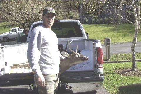 1995 Ford Bronco - A man stands next to the open tailgate of a pickup truck, with a deer carcass loaded inside. Another pickup truck is visible in the backgro…