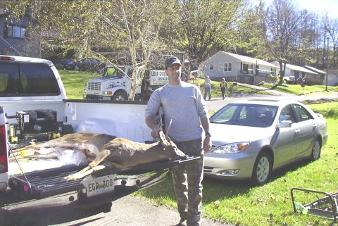 1995 Ford Bronco - A hunter displays his catch next to a pickup truck, with a sedan parked on the grass.