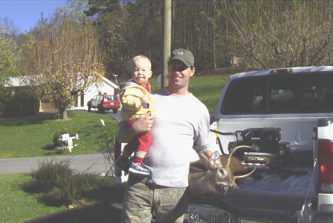 1995 Ford Bronco - A man holds a baby next to a pickup truck with a deer in the bed.