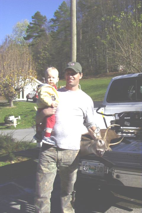 1995 Ford Bronco - A man proudly displays a deer in the back of his truck, with a baby in his arms.