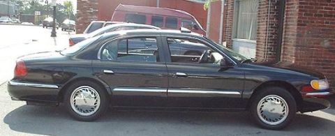 1997 Ford Crown Victoria - Side view of a black sedan parked on a street with a brick building in the background.
