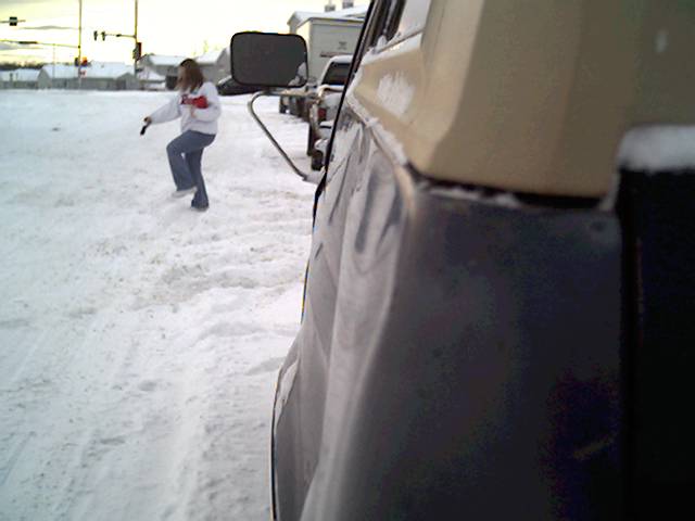 Person standing in snow next to the side of a dark-colored vehicle with a tan top