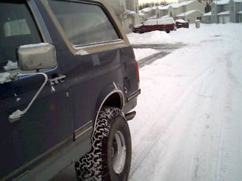 1987 Ford Bronco - Side view of a 1987 Ford Bronco parked in the snow, with a red SUV visible in the distance.