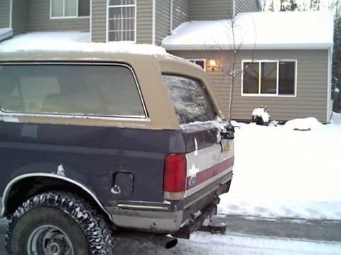 1987 Ford Bronco - A blue and tan Ford Bronco sits covered in snow in front of a house.