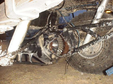 1988 Ford Bronco - The exposed rear differential and suspension components of a heavily modified vehicle are caked in mud.