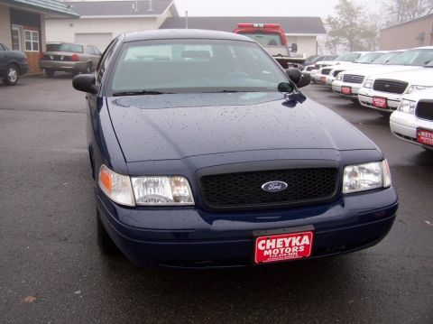 2001 Ford Crown Victoria - A dark blue 2001 Ford Crown Victoria is parked in front of a dealership, with other vehicles visible in the background.