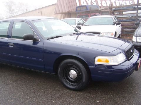 2001 Ford Crown Victoria - A dark blue 2001 Ford Crown Victoria sedan is parked in front of a building with other vehicles visible.