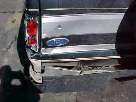 1993 Ford Bronco - The rear of a dark SUV shows significant damage to the bumper and taillight assembly, indicating a rear-end collision.