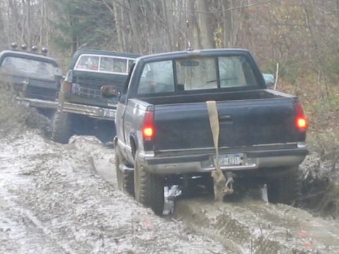 1994 Ford Bronco - Multiple trucks are stuck in the mud on a trail, with trees in the background.