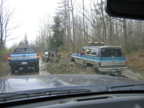 1994 Ford Bronco - Several vehicles navigate a challenging muddy path in a wooded area.