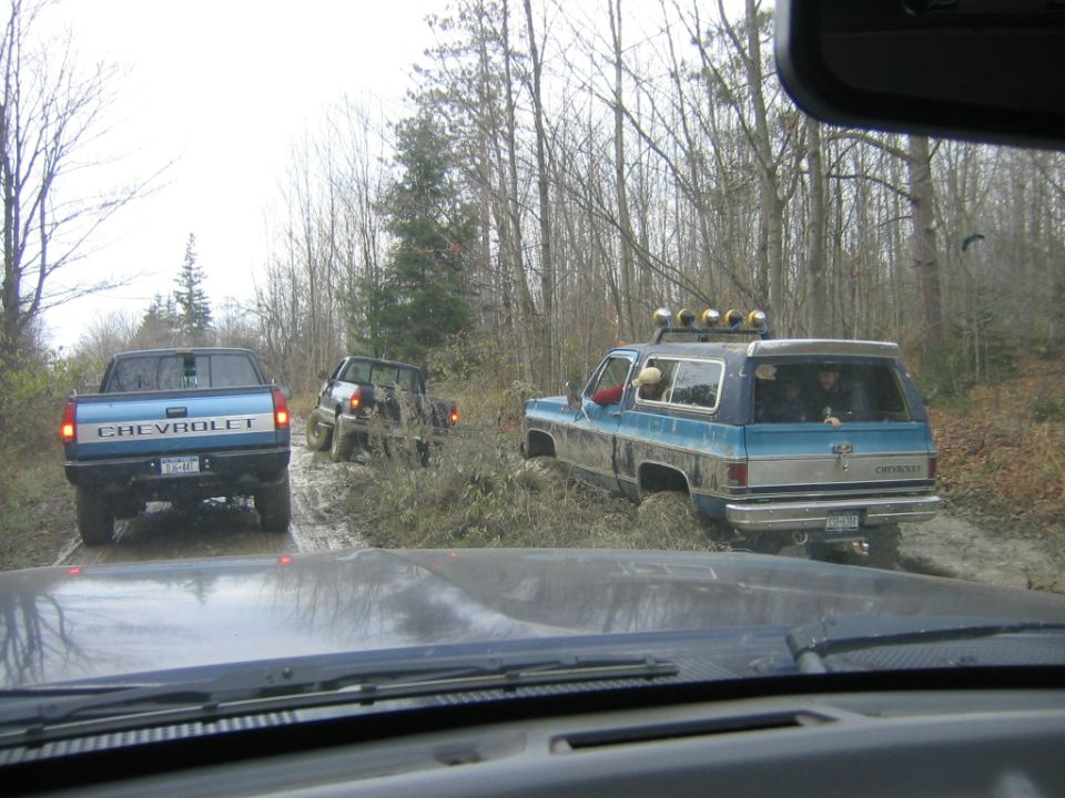 Blue Chevrolet K5 Blazer and a blue Chevrolet pickup truck driving on a muddy trail through trees