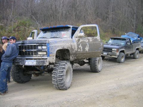 1994 Ford Bronco - A heavily mud-covered, lifted 1980 Chevrolet K5 Blazer is parked on a dirt road, with another pickup truck behind it.