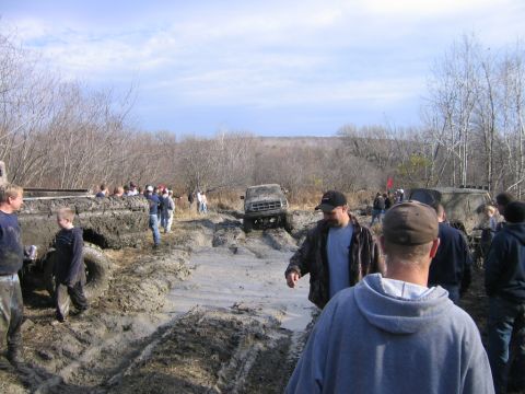 1994 Ford Bronco - A group of people watch as off-road vehicles navigate a muddy track during an event.