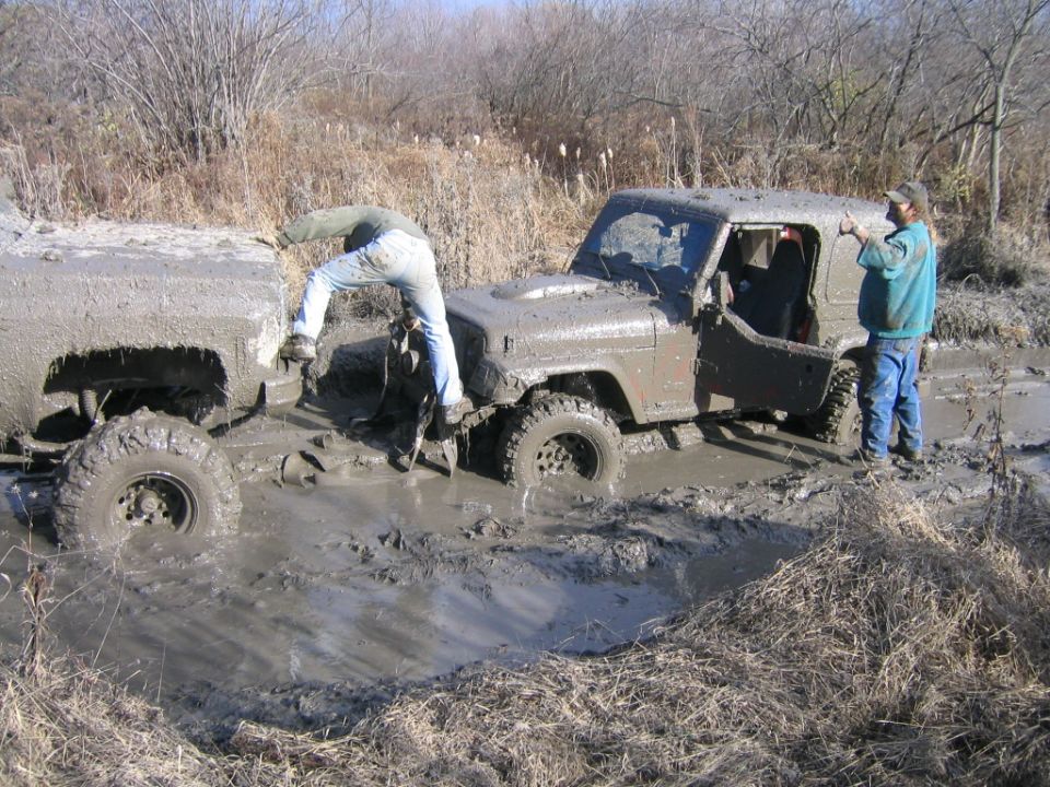Muddy off-road vehicles stuck in swamp; people attempting rescue