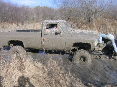 1994 Ford Bronco - Pickup truck stuck deep in mud with a person attempting to free it.