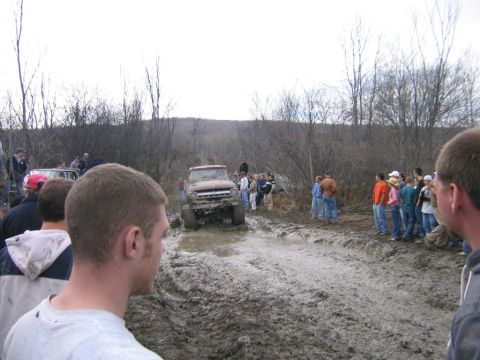 1994 Ford Bronco - A group of people watch as a mud-splattered Ford Bronco drives through a challenging off-road course.