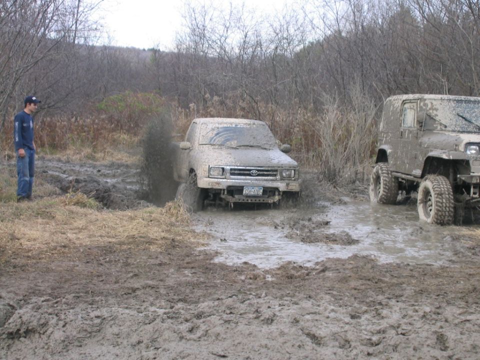 Mud-covered truck stuck in a muddy field with a person watching