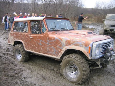1994 Ford Bronco - Muddy Jeep CJ-8 Scrambler off-roading with spectators nearby. Another vehicle is visible in the background.