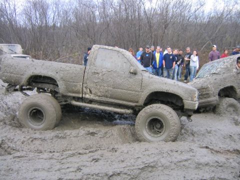 1994 Ford Bronco - Off-road vehicles navigate a challenging mud course, drawing a crowd of spectators.