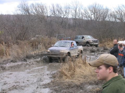 1994 Ford Bronco - Several vehicles navigate a muddy off-road course with onlookers present.