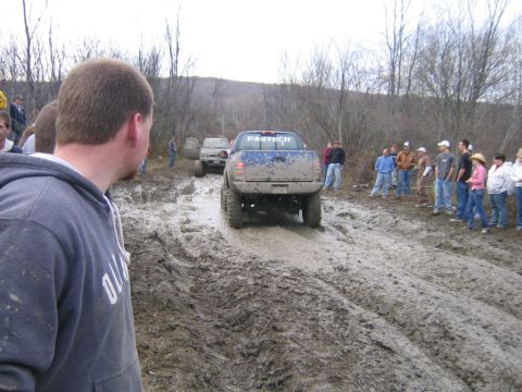 1994 Ford Bronco - Off-road trucks navigate a muddy track with onlookers observing the event.