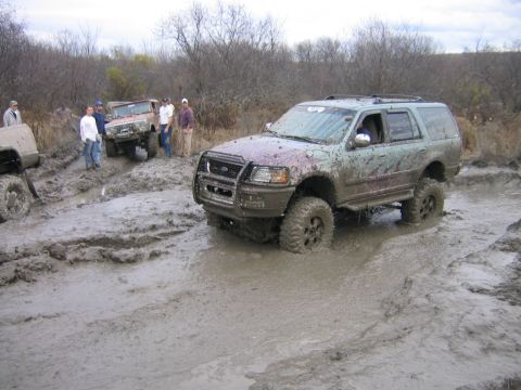 1994 Ford Bronco - Several off-road vehicles navigate a muddy terrain, with one Ford Expedition deeply mired in the muck.