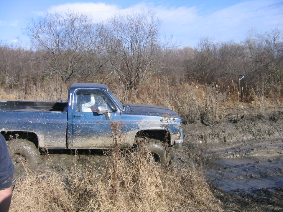 Blue pickup truck stuck in mud, front fender missing, side view