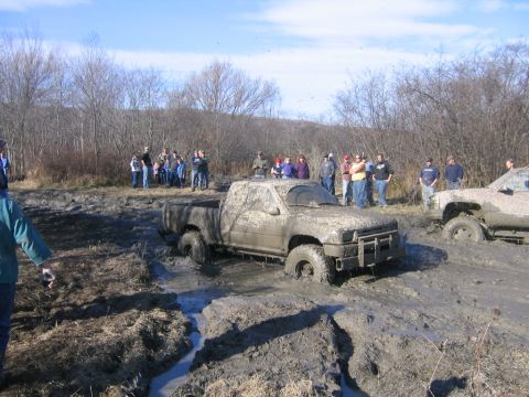 1994 Ford Bronco - Off-road vehicles stuck in thick mud during an event, with spectators observing the scene.