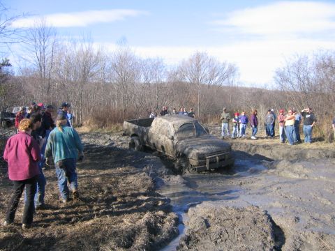 1994 Ford Bronco - A group of onlookers watch as a heavily mud-caked pickup truck struggles in a muddy terrain.
