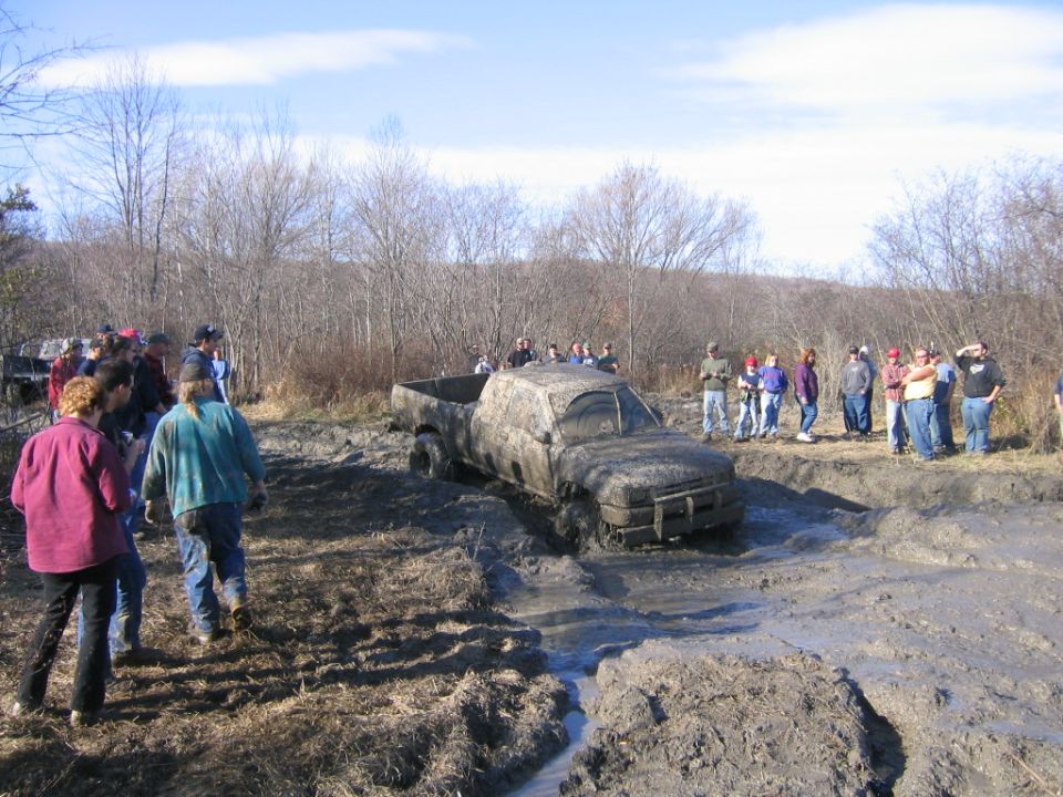 Muddy pickup truck stuck in a mud pit with people watching