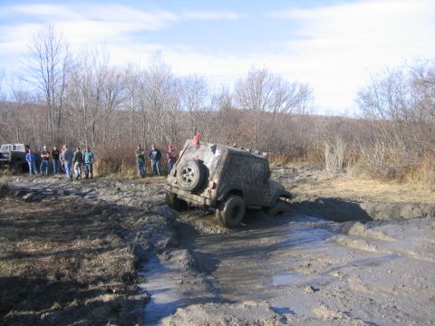 1994 Ford Bronco - A group of people watch as an off-road vehicle navigates a challenging mud pit during an event.