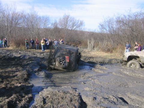 1994 Ford Bronco - A group of people watch as two vehicles struggle to get through a muddy off-road course.