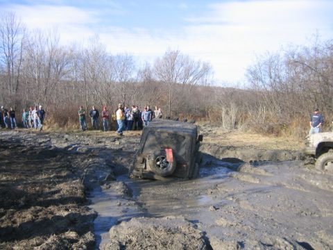 1994 Ford Bronco - Off-road vehicles are stuck in a muddy track while spectators observe the scene.
