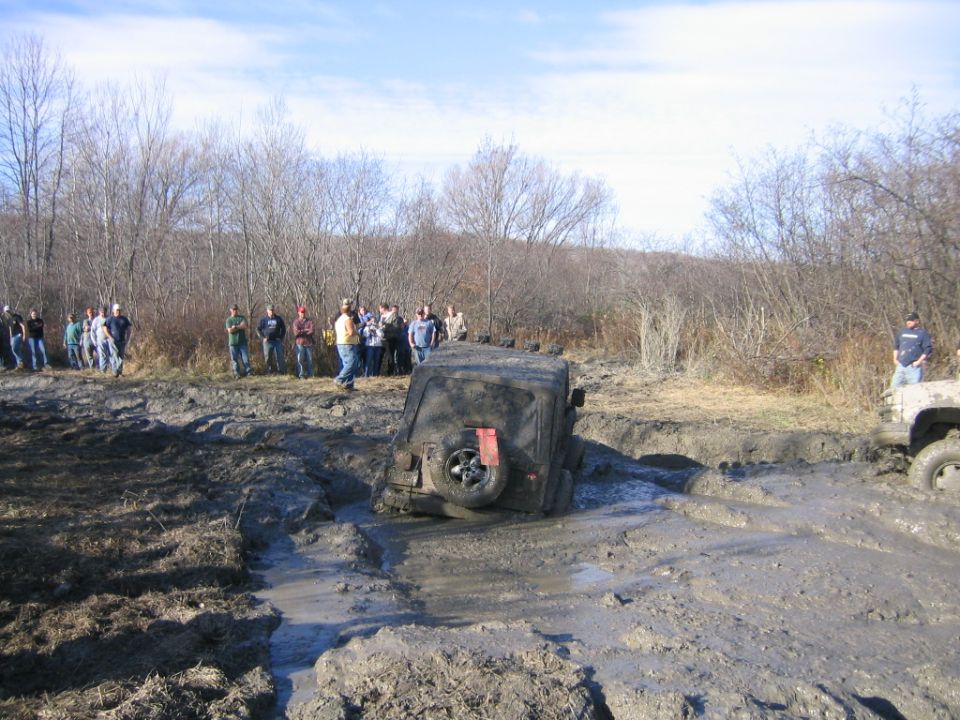 Muddy off-road vehicles stuck in a muddy track with spectators watching