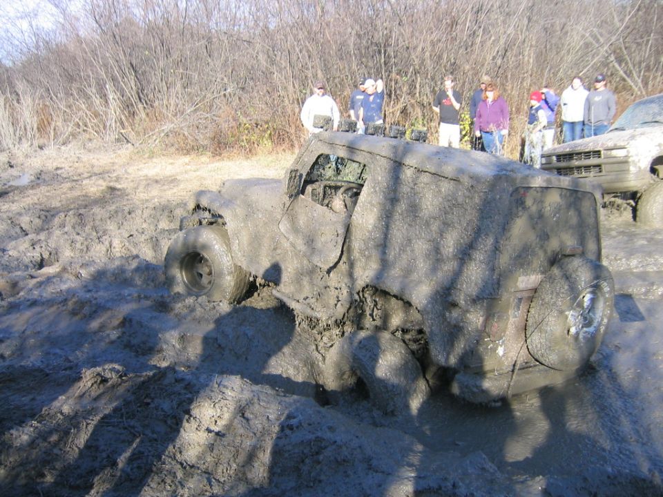 Mud-covered off-road vehicle stuck in mud with people watching