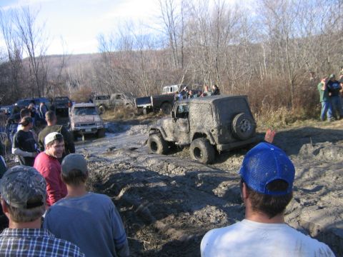 1994 Ford Bronco - Several off-road vehicles are stuck in the mud during an event, with onlookers observing the scene.