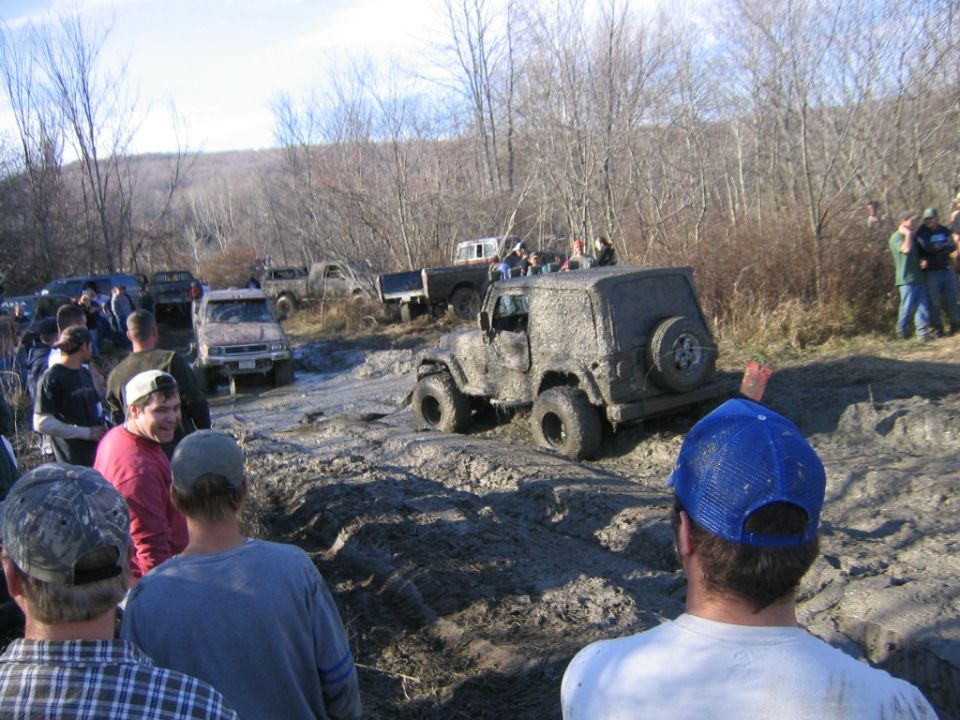 Muddy off-road vehicles navigating a muddy track with spectators watching
