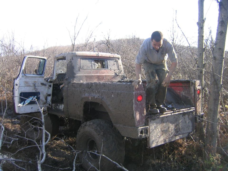 Mud-covered pickup truck with open driver's door, man climbing into the bed