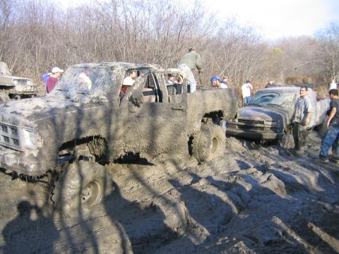 1994 Ford Bronco - Several trucks are stuck deep in mud during an off-road event.