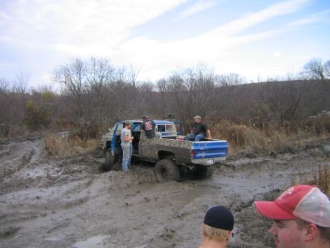 1994 Ford Bronco - People stand around a blue pickup truck that is stuck in a muddy field.