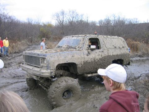 1994 Ford Bronco - Muddy K5 Blazer stuck in a muddy off-road course with onlookers.