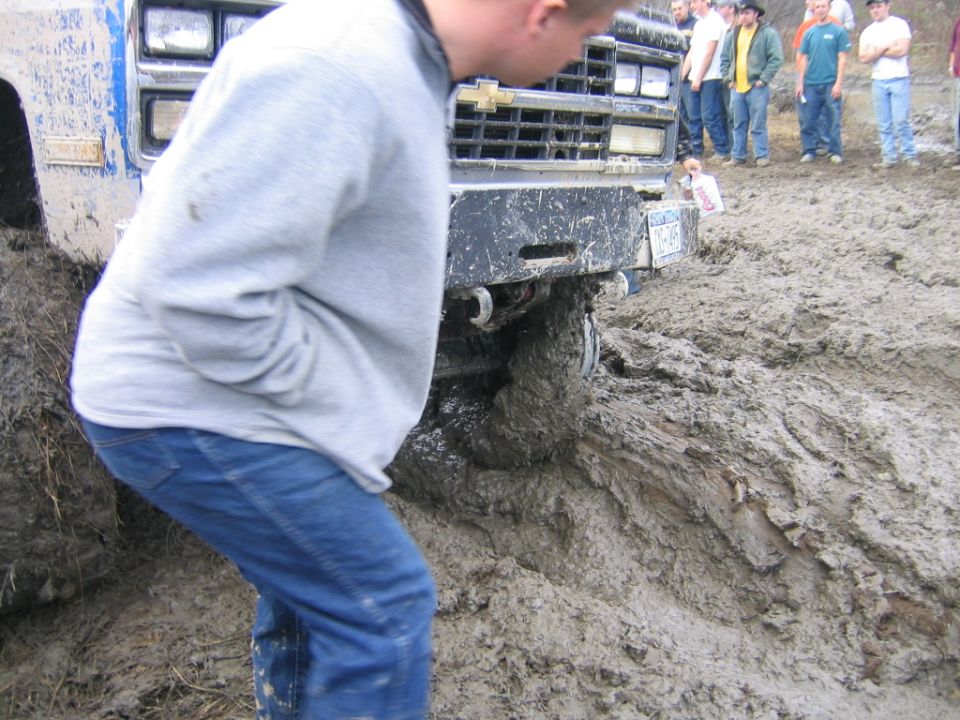 guy looking at truck stuck in mud, other people watching