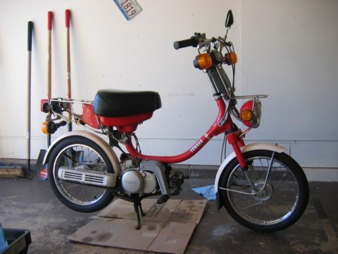 1985 Ford LTD Crown Victoria - A red and white Yamaha moped is parked on cardboard in a garage, with cleaning tools in the background.