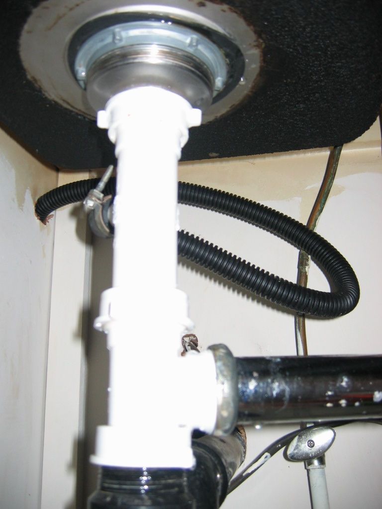 Plumbing pipes under a sink, showing a white P-trap and black corrugated hose connected to a metal drain flange