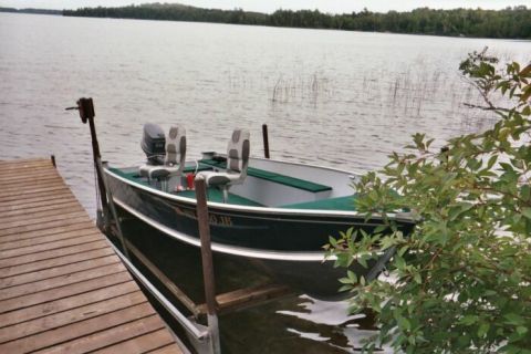 1996 Ford Bronco - A dark green fishing boat is tied to a wooden dock on a calm lake, with reeds in the background.