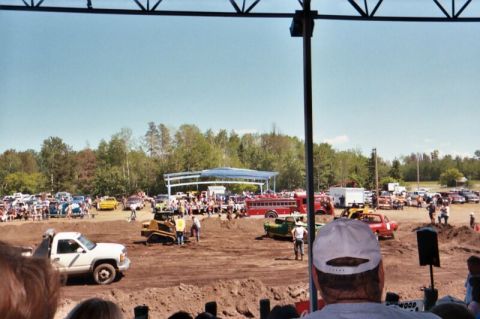 1996 Ford Bronco - A demolition derby event features a bulldozer, a fire truck, and many cars gathered in a dirt arena with spectators watching.