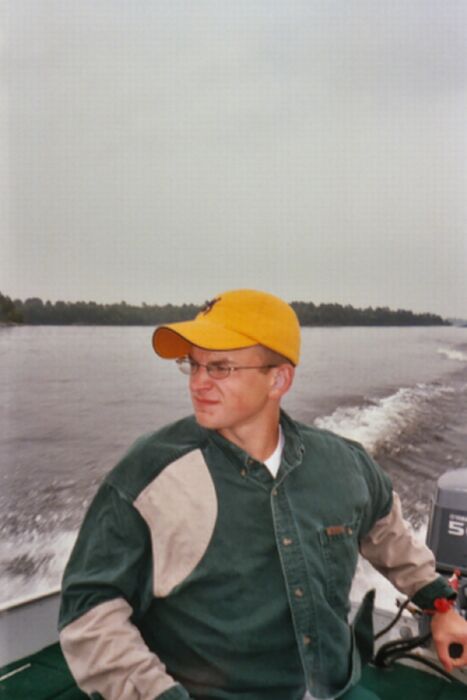 1996 Ford Bronco - A person in a yellow ball cap and green-and-tan jacket sits at the tiller of a small aluminum fishing boat under way, hand on the throttle…