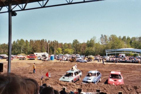 1996 Ford Bronco - Cars are bogged down in the dirt at a demolition derby event, with an audience watching from bleachers.