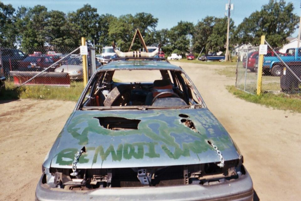 Damaged car with holes in hood, green paint, and chains attached